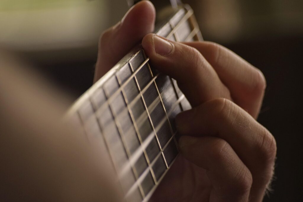 gClose-up of a person playing a guitar with discipline, focusing carefully on the strings and fretboard