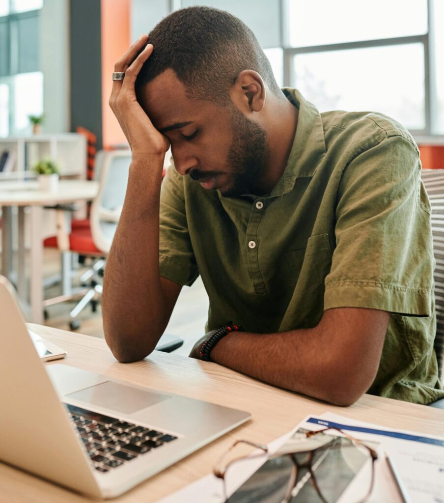 An exhausted office worker sitting at a laptop, holding their head in frustration after working hard for long hours