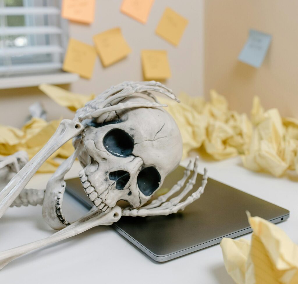 A small decorative skull wrapped in twine resting on a desk beside a keyboard, surrounded by sticky notes and office supplies.
