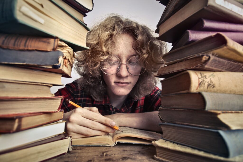 A person surrounded by towering stacks of books reads intently, immersed in learning.
